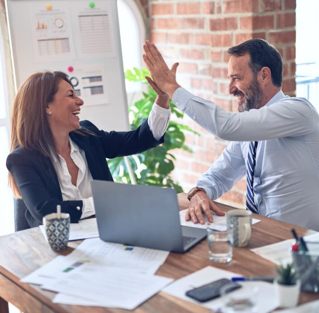 A man and a woman sitting at a table with their laptop and cheering